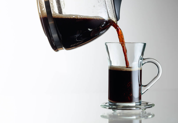 Café preto em uma xícara de vidro em uma mesa de vidro. O café é derramado da máquina de café em uma xícara. Espaço de cópia
. - Foto, Imagem