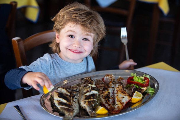 Hyvää hymyä. Terveellistä syömistä lapsille. Grillattua kalaa terveelliseksi illalliseksi. Poika hymyilee ravintolassa
. - Valokuva, kuva