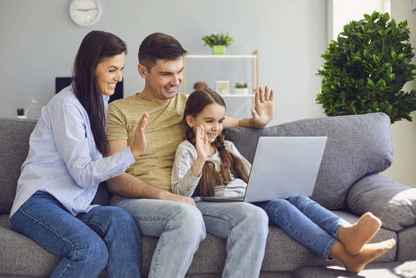 A happy family online communication using a laptop while sitting with the child on the couch at home - Foto, Bild
