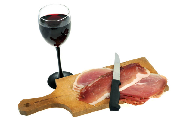 Tranches de jambon cru sur une planche à découper avec un verre de vin et un couteau sur fond blanc
 - Photo, image