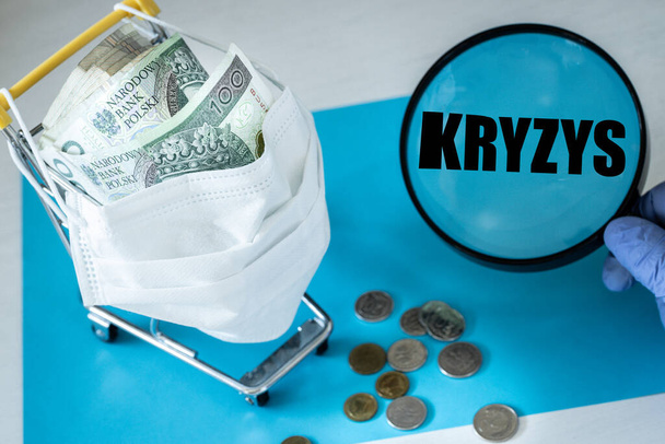 コロナウイルスに対するマスクの買い物用トロリー。ポーランドの金だ。ガラスの拡大、単語"KRYZYS"ポーランド語のテキスト。国の経済崩壊の概念 - 写真・画像