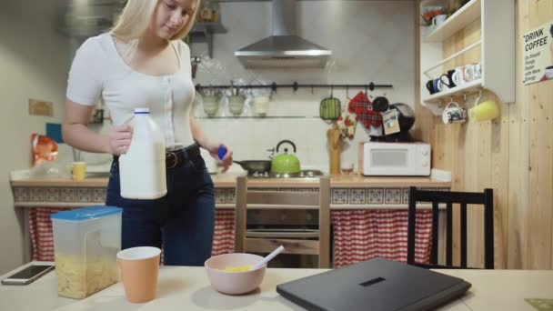 Young woman working laptop computer and eats Corn Flakes Cereal at home kitchen. - Materiał filmowy, wideo