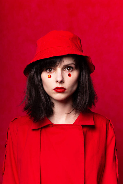 beautiful girl in red, with red lipstick on the lips and dots under the eyes - Photo, image