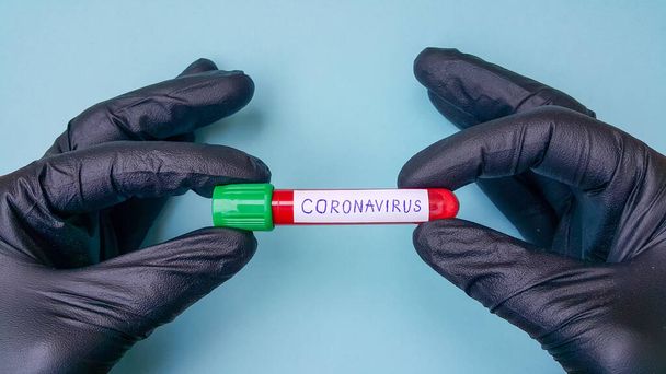 Коронавирус Covid-19 Вакуумные трубы для медицинской работы с образцами крови в лаборатории. Тест на коронавирус. Рука доктора в чёрной резиновой медицинской перчатке. Пространство для текста на синем фоне
. - Фото, изображение