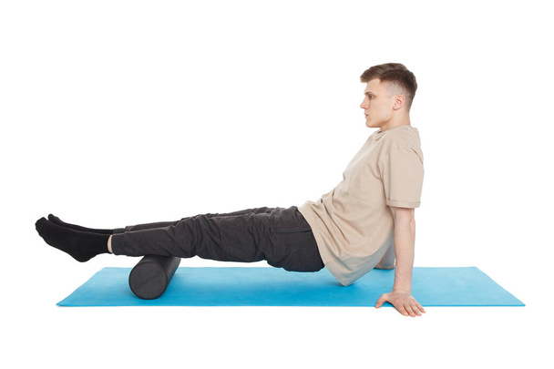 Handsome man shows exercises using a foam roller for a myofascial release massage of trigger points. Massage of the shin muscle. Isolated on white. - Φωτογραφία, εικόνα