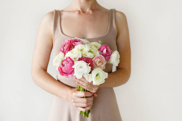 Konzeptbild einer Frau im modischen beigen Kleid mit Frühlingsblumen. Weibchen mit farbenfrohem weißen und rosa Hahnenstrauß auf weißem Hintergrund. Nahaufnahme, Kopierraum, Schnappschuss. - Foto, Bild