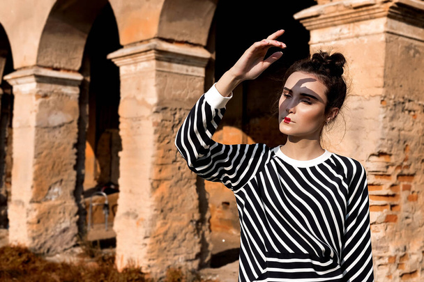 Beauty Fashion Model Girl with Brown Hair on a background of an old, abandoned building, wearing stylish clothes. Sexy woman portrait with perfect make-up and fashionable clothes. Beauty Trends - 写真・画像
