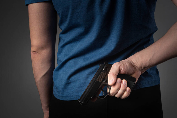 a man in a blue T-shirt pulls a gun behind his back - 写真・画像