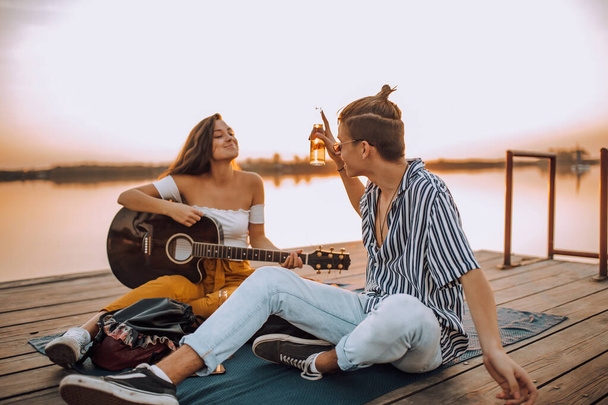 Happy young cheerful couple in love having fun by the river. Playing guitar and singing. - Photo, Image