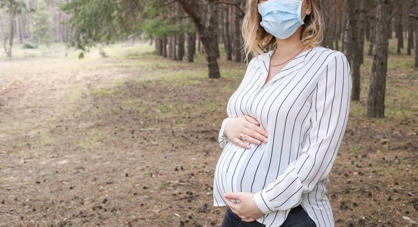Pregnant european girl with a medical mask. Coronavirus. Pandemic infectious concept and pregnancy. Copy space for text - Photo, Image