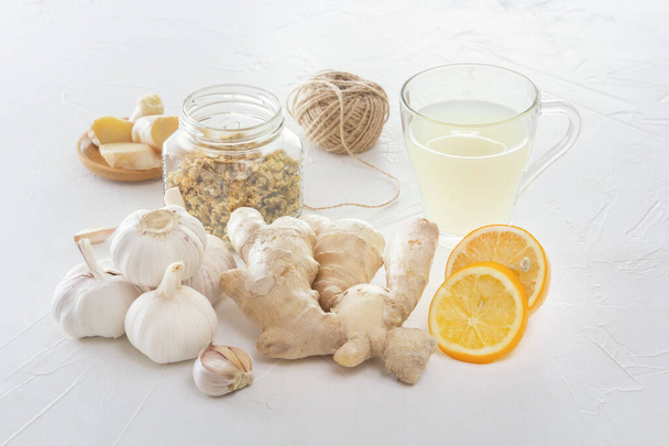 Ginger, garlic, lemon, dried medical chamomile in a jar and ginger tea - a means to protect against viral infections and colds on a light wooden table. - Photo, image