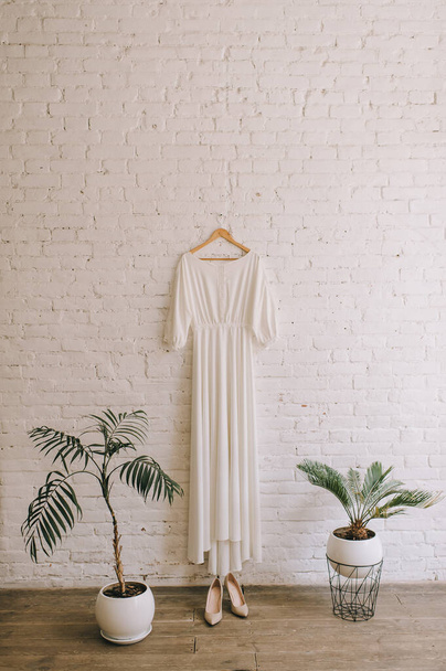 einfaches weißes Hochzeitskleid, das an einer weißen Ziegelwand hängt - Foto, Bild