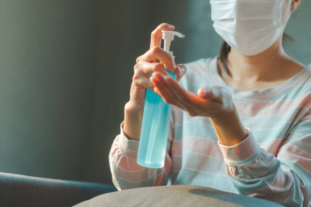 Donna che indossa una maschera protettiva per l'igiene medica per l'assistenza sanitaria da Coronavirus (COVID-19) quarantena a casa pulizia delle mani con gel. Assistenza sanitaria, quarantena e prevenzione del rischio di Coronavirus (COVID-19)
. - Foto, immagini