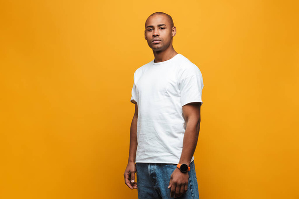 Portrait of an attractive confident casual young african man standing over yellow background - Foto, Imagen