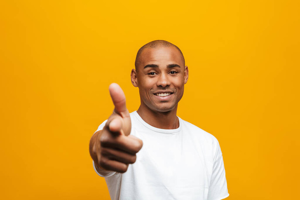 Portrait of an attractive smiling confident casual young african man standing over yellow background, pointing finger at camera - Foto, immagini