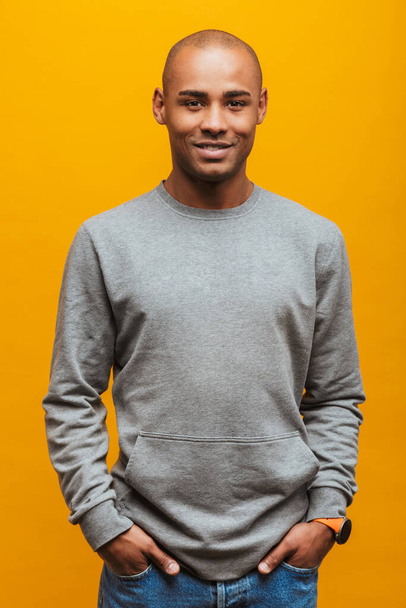 Portrait of an attractive confident casual young african man standing over yellow background, looking at camera - Foto, Imagen