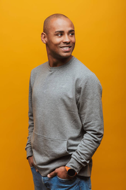 Portrait of an attractive confident casual young african man standing over yellow background, looking away - Foto, Imagem