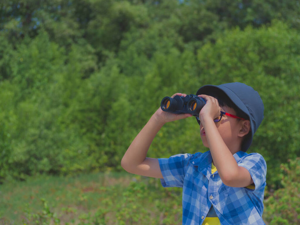 Young boy looking through binoculars on sunny summer day with happiness. - Фото, изображение