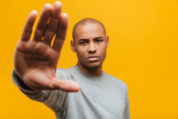 Portrait of an attractive confident casual young african man standing over yellow background, showing stop gesture - Foto, Bild