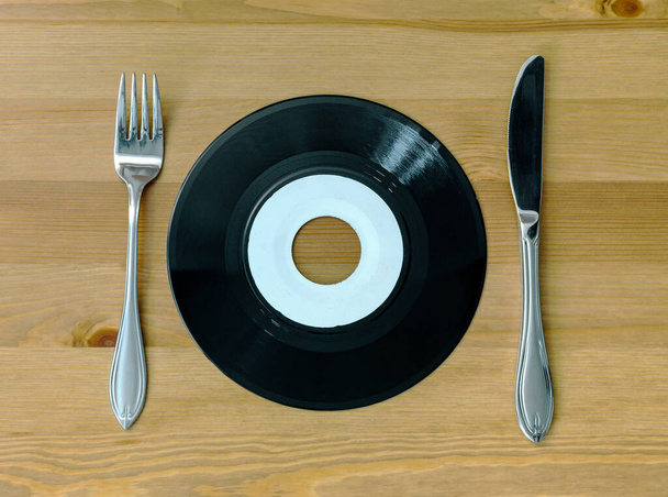 Plaka şeklinde, tahta arka planda gümüş bıçak ve çatal, müzik ve yiyecek konsepti olan 7 inçlik siyah vinil plak. - Fotoğraf, Görsel