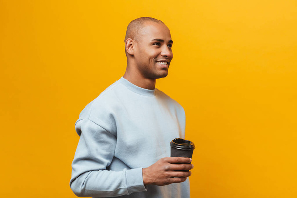 Portrait of an attractive smiling confident casual young african man standing over yellow background, holding takeaway coffee - Foto, imagen
