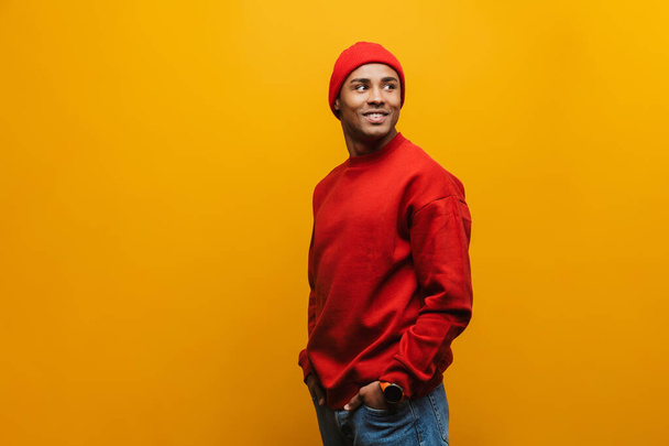 Portrait of an attractive smiling confident casual young african man standing over yellow background, looking away - Fotografie, Obrázek