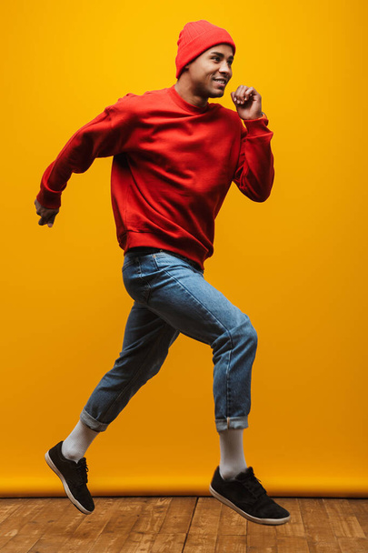 Full length portrait of an attractive happy confident casual young man jumping over yellow background - Zdjęcie, obraz