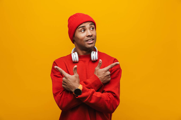 Portrait of an attractive confident casual young african man standing over yellow background, pointing sideways - Фото, изображение
