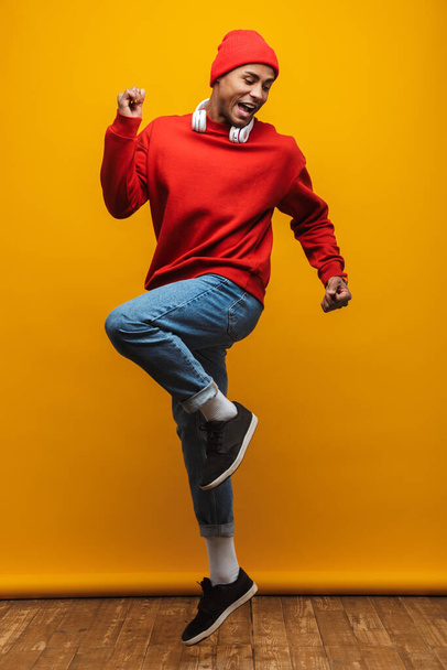 Full length portrait of an attractive happy confident casual young african man jumping over yellow background - Φωτογραφία, εικόνα