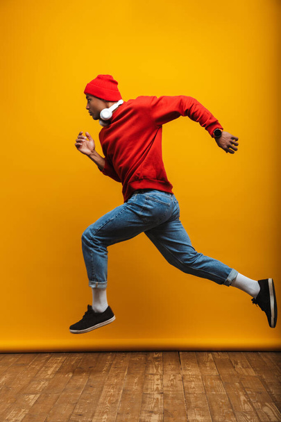 Full length side view portrait of an attractive confident casual young african man running over yellow background - Fotografie, Obrázek