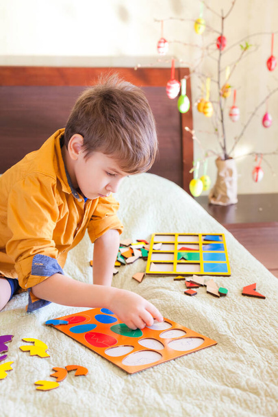 Little kid collects easter puzzle at bed in home interior. Easter decoration in the background - Photo, Image