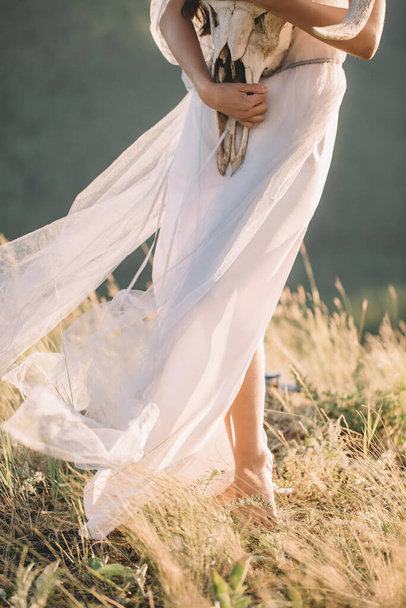 Beautiful legs girl in a white winding in the wind dress, with grass in hand, the horns of the deer from below, closeup, nature, mountains, forest - Foto, Imagem