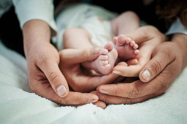 Pair of hans holding legs of newborn baby - Foto, Imagem
