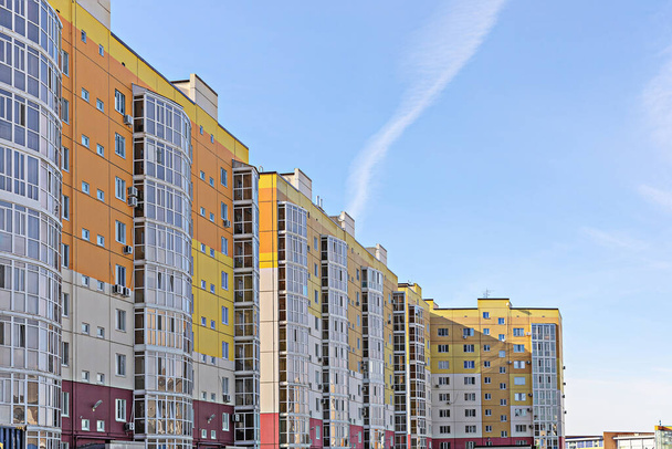 Vista de un nuevo edificio de varios pisos sobre un fondo de cielo azul. Las paredes del edificio están pintadas en naranja, rojo y blanco
 - Foto, Imagen
