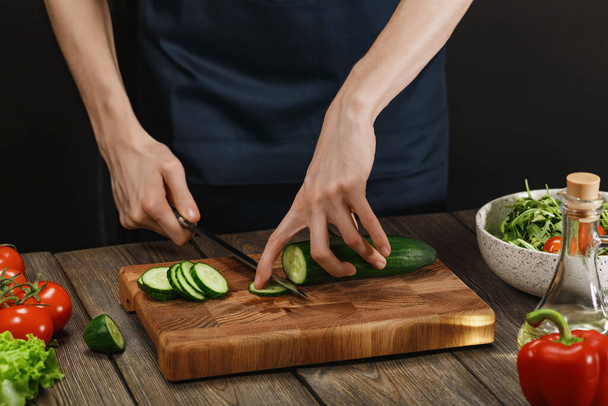 新鮮な健康的なサラダを作る女性.木のテーブルの上で野菜を切る女性の手. - 写真・画像