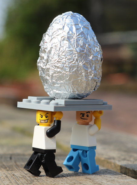 Két Lego ember elvisz egy ezüst húsvéti tojást a napon. - Fotó, kép