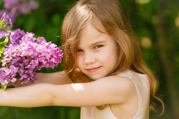 small girl in near a lilac flowers  with bouquet - Foto, Imagen