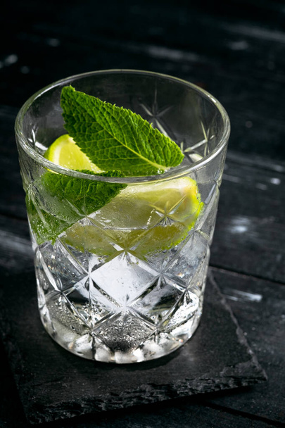 Gin and Tonic cocktail with lime, mint and ice, alcoholic drink in a glass on a dark wooden background, close up - Foto, Bild
