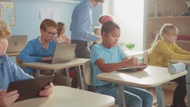 Klasa informatyki szkolnej: Dziewczyna używa komputera z cyfrowym tabletem, Jej koledzy z klasy pracują z laptopami, Nauczyciel idzie w klasie pomagając dzieciom. Dzieci coraz nowoczesnej edukacji w STEM, gry i uczenia się - Materiał filmowy, wideo