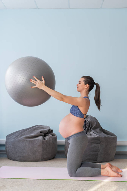 Pregnant caucasian woman on fitness with a ball. Yoga for expectant mothers. Girl in the classroom in preparation for childbirth. Pilates in the last trimester. - Фото, зображення