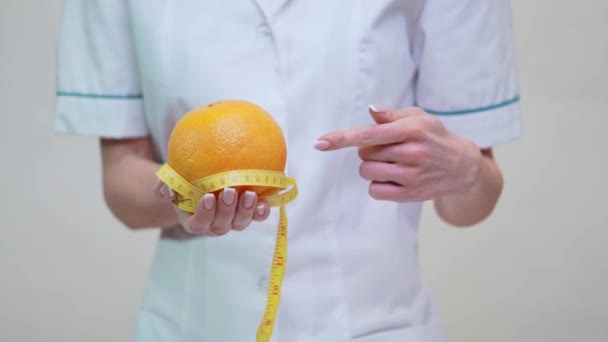 nutritionist doctor healthy lifestyle concept - holding orange fruit and measuring tape - Video, Çekim