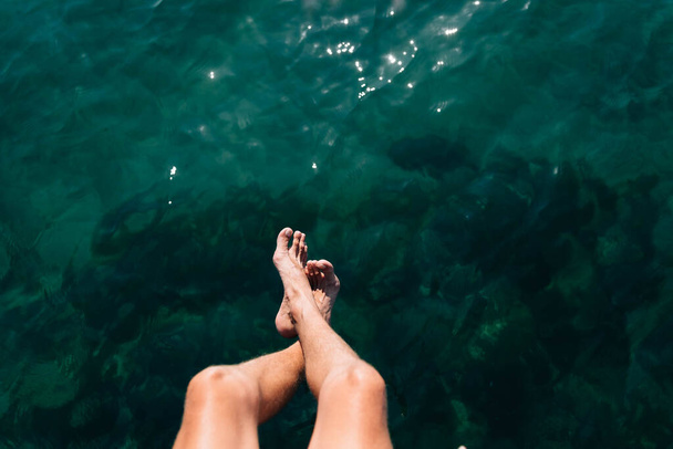 Männerbeine auf dem Hintergrund des Ozeans. Ruhen Sie sich im Sommer im Resort aus. Platz für Text - Foto, Bild