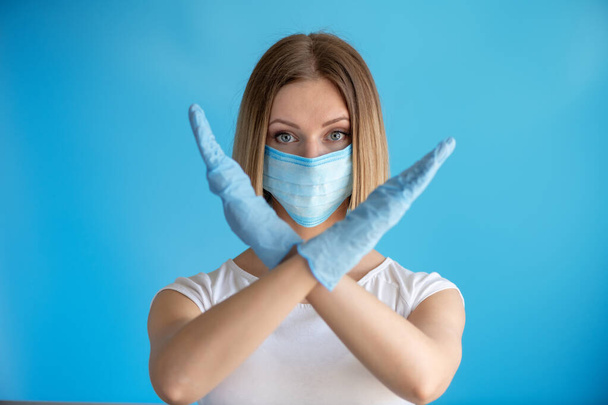 Attractive female nurse showing stop sign with his hand gesture isolated on blue background. Medical concept of infection - Photo, Image