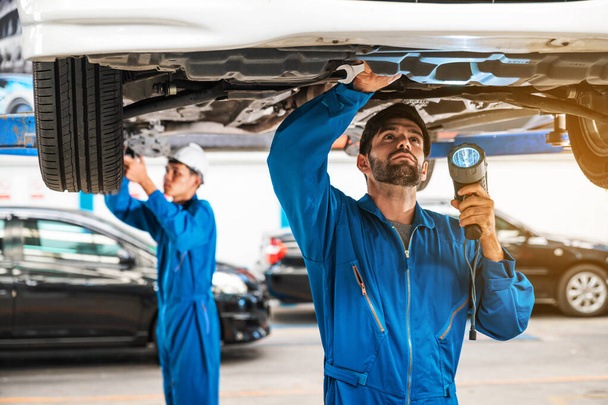 Mechaniker und sein Assistent untersuchen den Wagenboden mit Blitzlicht. Auto-Reparatur-Service-Center. Professioneller Service. - Foto, Bild