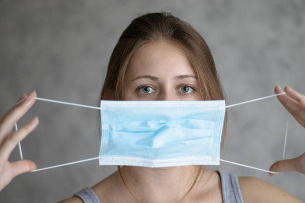 Beautiful young woman holding face mask because of air pollution, coronavirus or flu. Girl puts on a medical mask. Method of preventing an epidemic or pandemic of the virus. - Fotografie, Obrázek