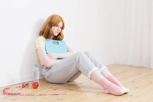 smutna nastolatka dziewczyna z wagi na drewnianej podłodze - Zdjęcie, obraz