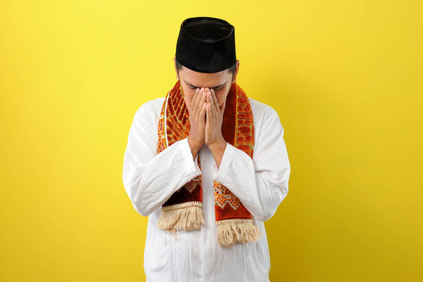 Young Asian Muslim man feel sad with covering his face with hands. Copy space concept, isolated on yellow background - Фото, изображение