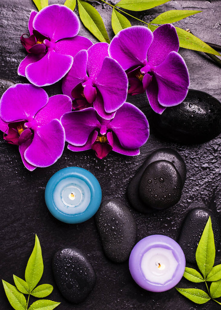 濃い背景に紫色の蘭の花、葉や香りのキャンドルを持つ黒い石のグループ - 写真・画像