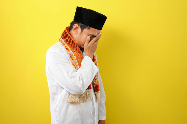 Młody muzułmanin azjatycki smuci się zakrywając twarz rękami. Koncepcja przestrzeni kopiującej, izolowana na żółtym tle - Zdjęcie, obraz