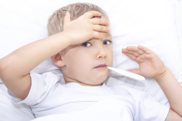boy lies in bed with a thermometer in his mouth. healthcare concept and sick child, coronavirus, high fever, - Foto, imagen